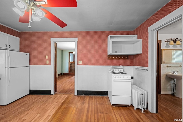 408 E Henry St, Atkinson, IL 61235 - kitchen with radiator, white appliances, light wood-style flooring, a ceiling fan, and a wainscoted wall