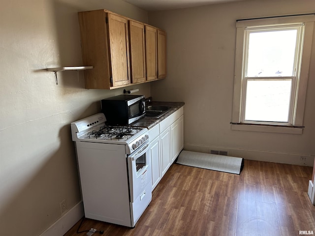 kitchen featuring white range with gas stovetop, visible vents, wood finished floors, a sink, and baseboards