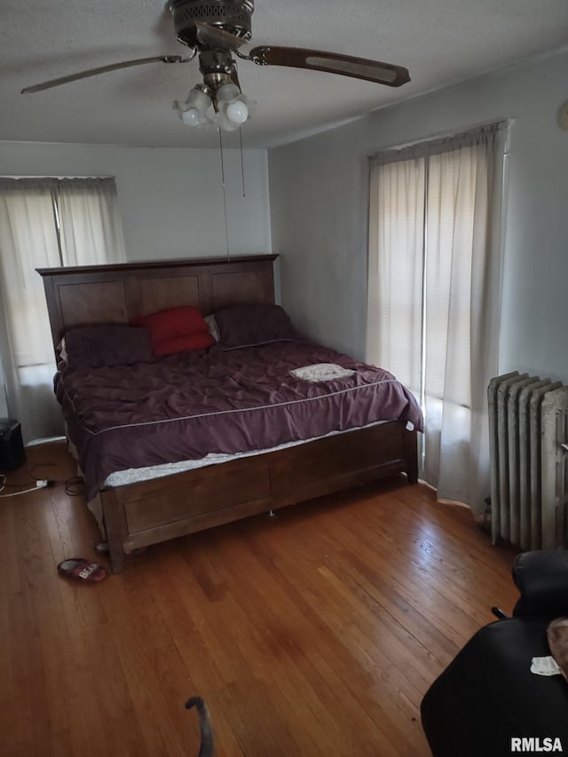 bedroom with a ceiling fan, radiator heating unit, wood finished floors, and a textured ceiling