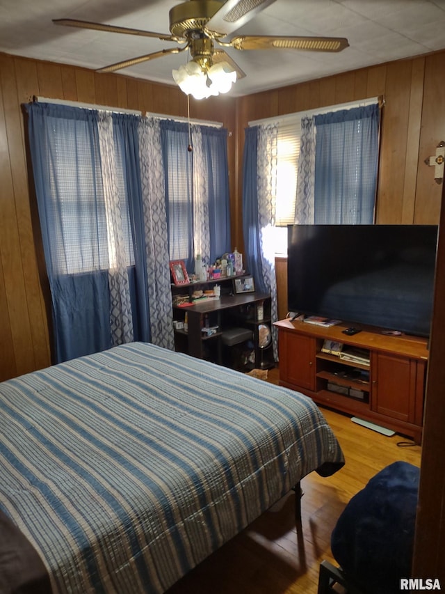 bedroom with wood walls, wood finished floors, and a ceiling fan