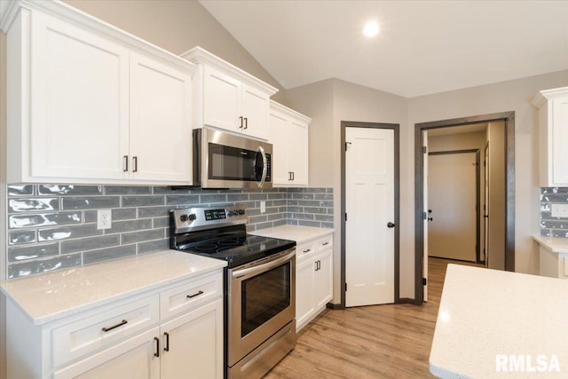 kitchen with light wood-style floors, white cabinetry, vaulted ceiling, appliances with stainless steel finishes, and backsplash