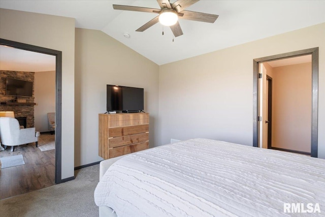 bedroom with carpet flooring, a stone fireplace, vaulted ceiling, and a ceiling fan