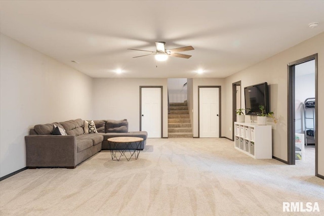 living area featuring ceiling fan, light colored carpet, baseboards, and stairs