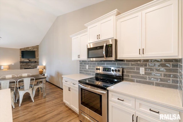 kitchen featuring decorative backsplash, light wood-style flooring, vaulted ceiling, and appliances with stainless steel finishes