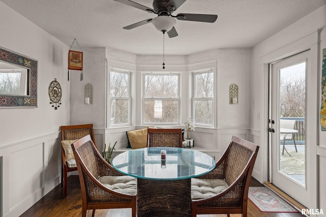 dining space with a textured ceiling, a ceiling fan, wainscoting, dark wood finished floors, and a decorative wall