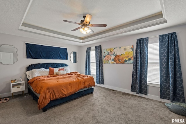 carpeted bedroom with a tray ceiling, a textured ceiling, baseboards, and a ceiling fan
