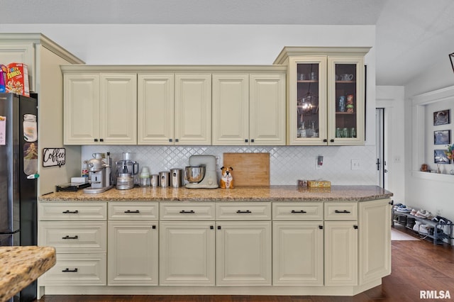 kitchen with tasteful backsplash, freestanding refrigerator, and light stone counters