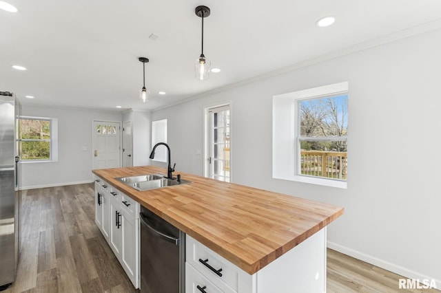 kitchen with butcher block countertops, white cabinetry, a sink, and crown molding