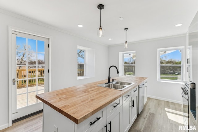 kitchen featuring butcher block countertops, white cabinetry, a kitchen island with sink, stainless steel dishwasher, and a sink