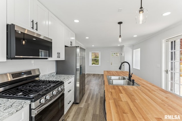 kitchen featuring light wood-style flooring, crown molding, butcher block counters, appliances with stainless steel finishes, and a sink