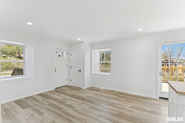 interior space with light wood-style flooring, crown molding, a healthy amount of sunlight, and baseboards