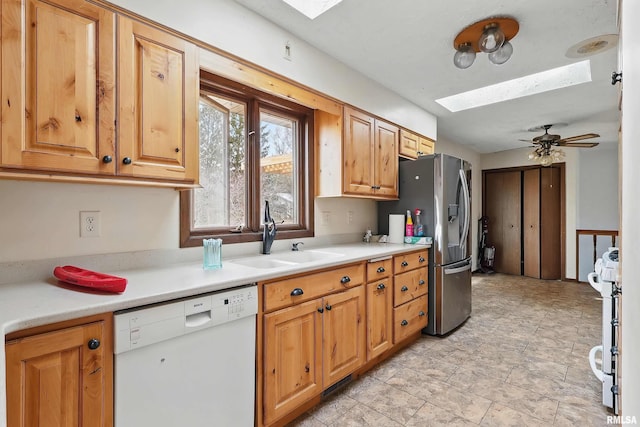 kitchen featuring a sink, light countertops, a skylight, and white appliances