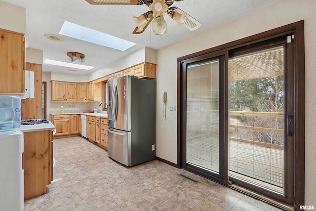 kitchen featuring stainless steel fridge with ice dispenser, light countertops, a ceiling fan, a skylight, and white dishwasher
