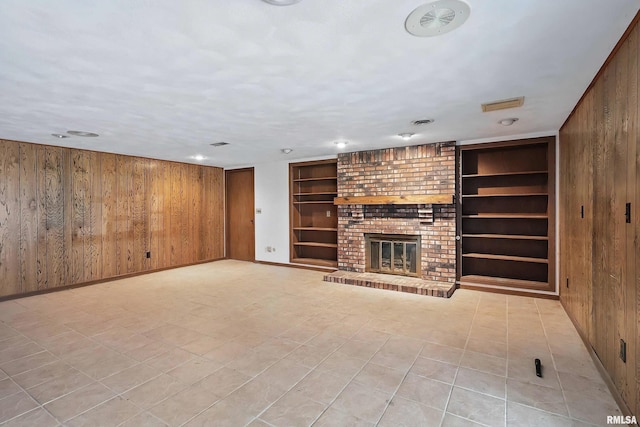 unfurnished living room featuring built in features, wood walls, baseboards, and a brick fireplace