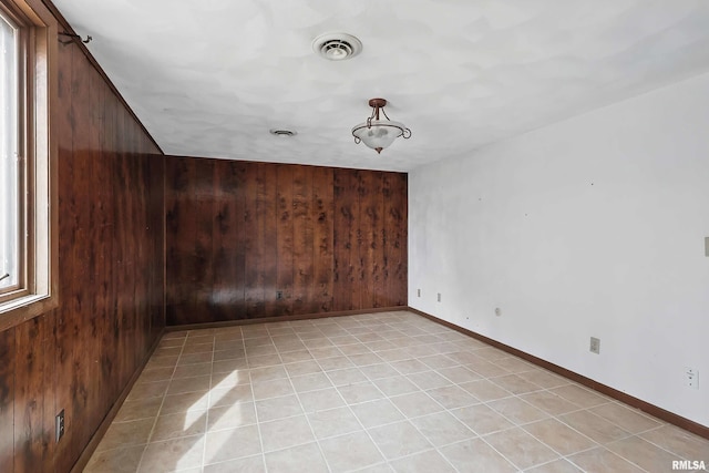 unfurnished room featuring wooden walls, visible vents, baseboards, and light tile patterned floors