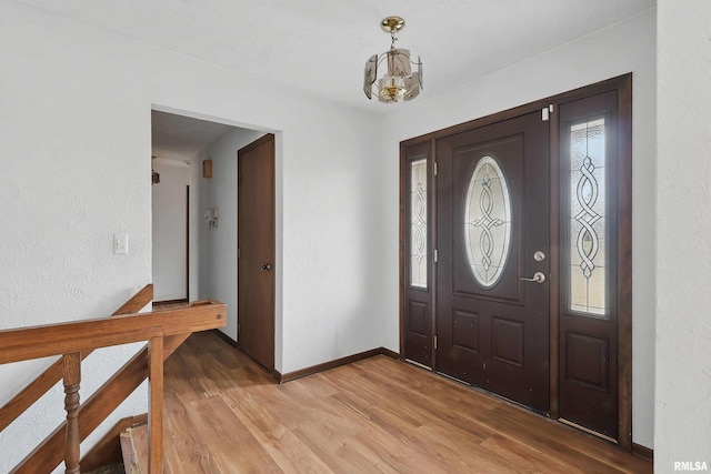 foyer entrance with baseboards, a notable chandelier, and light wood-style floors