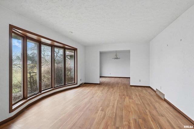 unfurnished room with light wood-style floors, an inviting chandelier, baseboards, and a textured ceiling