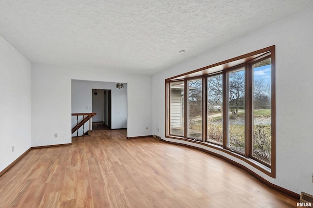 empty room with baseboards, light wood-type flooring, and a textured ceiling