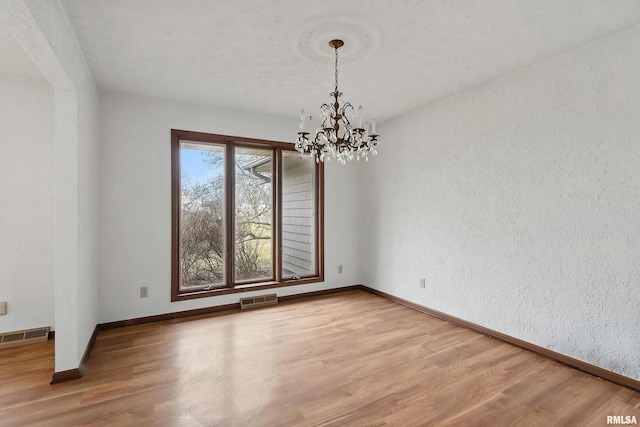 unfurnished room with a chandelier, light wood finished floors, visible vents, and baseboards