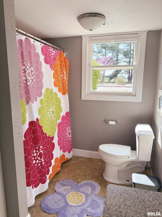 bathroom featuring baseboards, a textured ceiling, a shower with shower curtain, and toilet