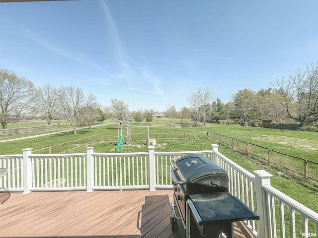 wooden deck with a lawn, fence, a rural view, and a playground