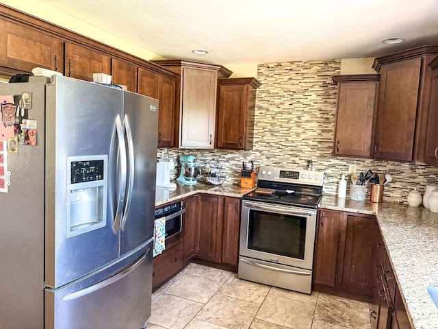 kitchen with light tile patterned flooring, light stone countertops, appliances with stainless steel finishes, and decorative backsplash