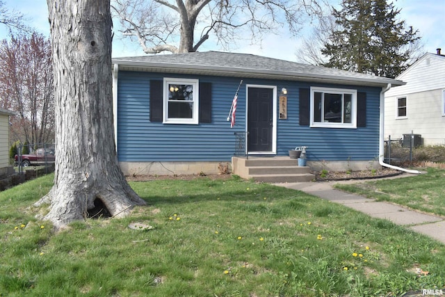 bungalow-style home with roof with shingles, central AC, and a front lawn