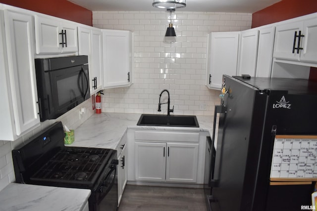 kitchen featuring light stone counters, a sink, white cabinets, black appliances, and backsplash