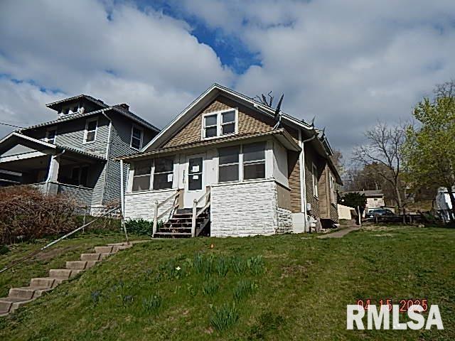 view of front of home with stone siding, entry steps, and a front yard