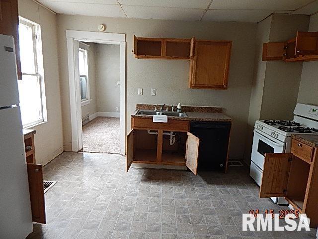 kitchen featuring dark countertops, a sink, white appliances, baseboards, and brown cabinetry