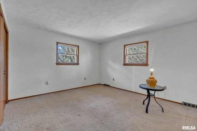 carpeted empty room featuring baseboards, visible vents, and plenty of natural light