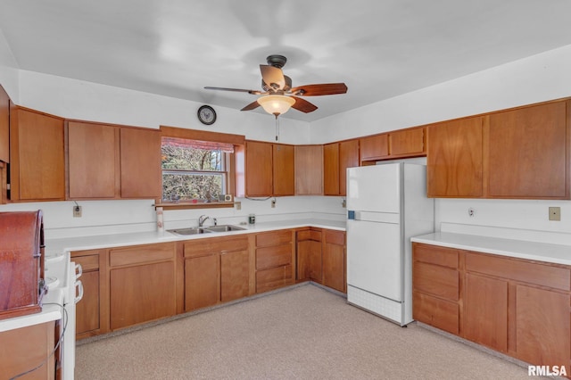 kitchen with a sink, freestanding refrigerator, brown cabinets, ceiling fan, and light countertops