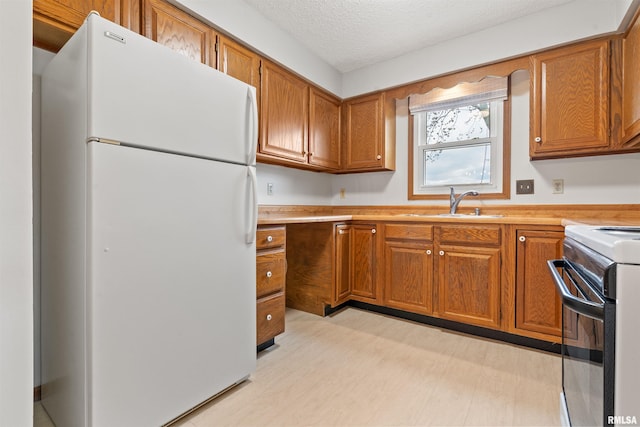 kitchen featuring freestanding refrigerator, brown cabinetry, a sink, and electric range oven