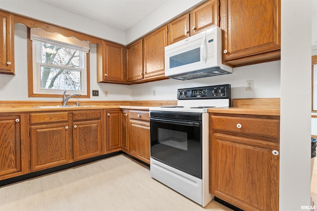 kitchen featuring a sink, brown cabinets, white microwave, light countertops, and electric range