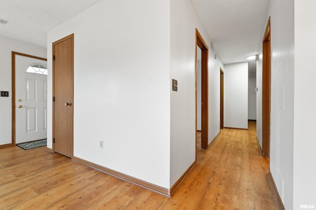 corridor featuring baseboards, light wood-style floors, and visible vents