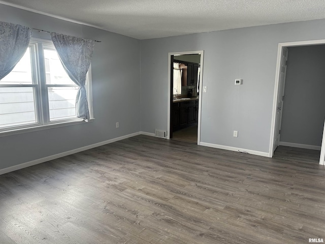 unfurnished bedroom featuring a textured ceiling, ensuite bathroom, visible vents, baseboards, and dark wood-style floors