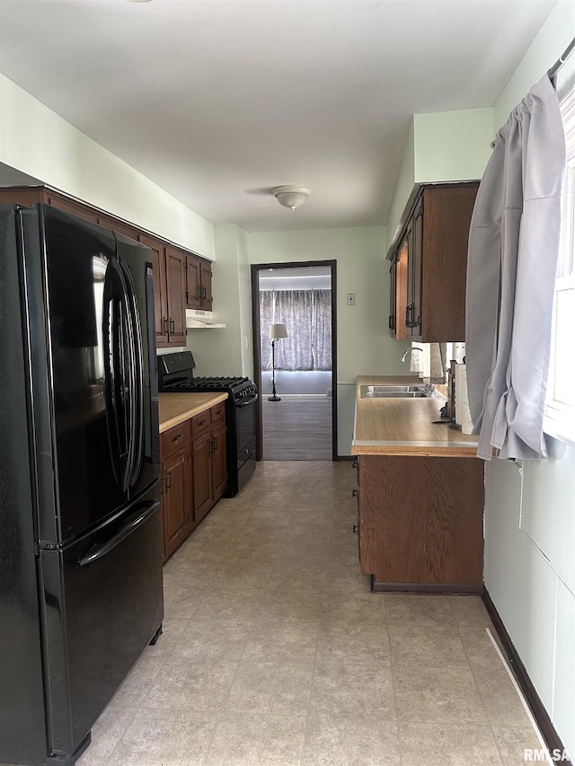 kitchen with a sink, dark brown cabinetry, light countertops, under cabinet range hood, and black appliances