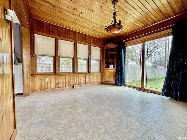 spare room with wood ceiling, wood walls, visible vents, and baseboards