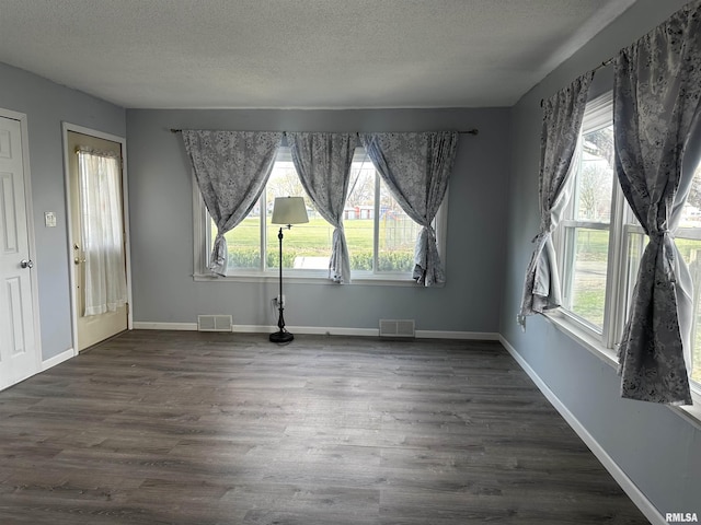 unfurnished dining area featuring dark wood-style floors, a textured ceiling, and visible vents