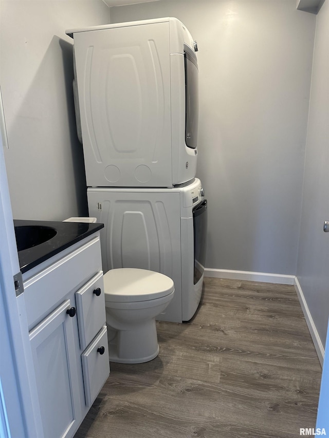 bathroom featuring stacked washer / drying machine, wood finished floors, toilet, vanity, and baseboards