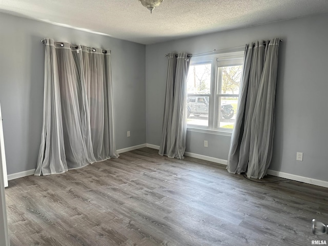 unfurnished room with wood finished floors, a textured ceiling, and baseboards