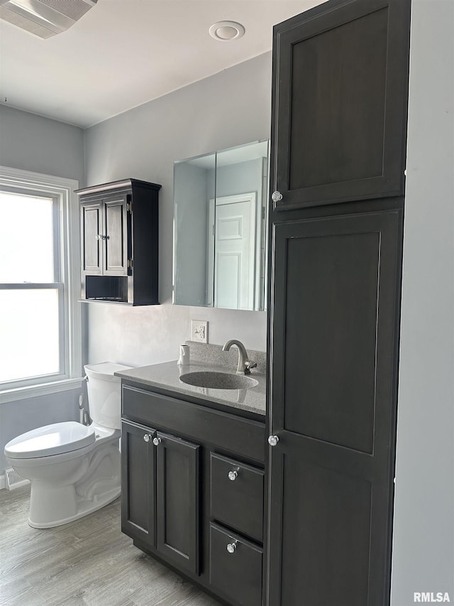 half bathroom with visible vents, wood finished floors, vanity, and toilet