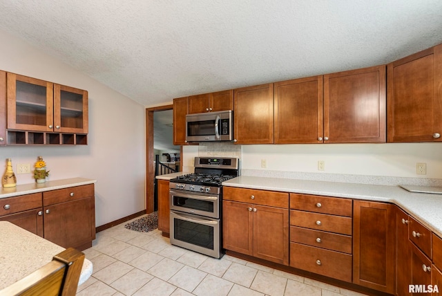 kitchen featuring a textured ceiling, glass insert cabinets, stainless steel appliances, light countertops, and lofted ceiling