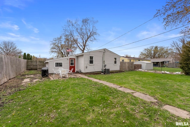 back of house with a fenced backyard, an outdoor structure, a yard, and a shed
