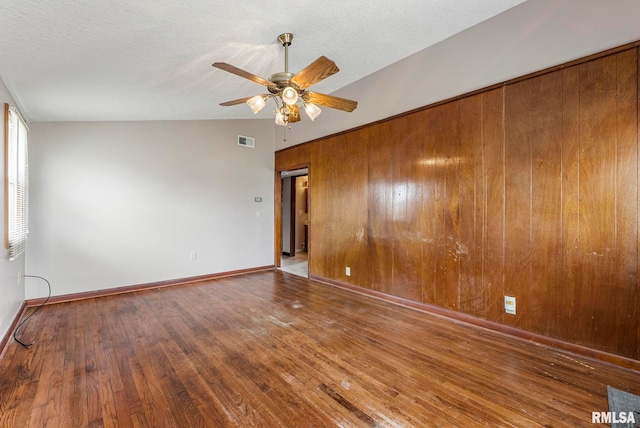 unfurnished room with a ceiling fan, wood finished floors, baseboards, wood walls, and visible vents