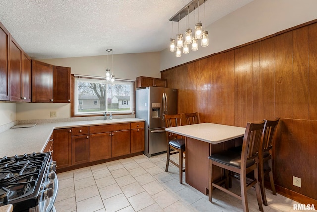 kitchen with vaulted ceiling, a textured ceiling, stainless steel appliances, light countertops, and a kitchen bar