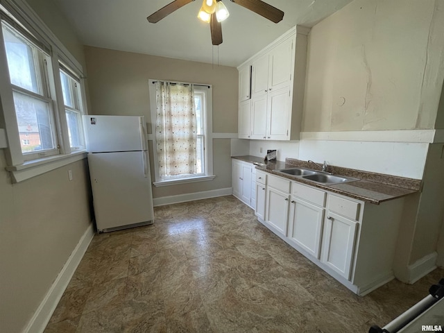 kitchen featuring a ceiling fan, a sink, baseboards, white cabinetry, and freestanding refrigerator