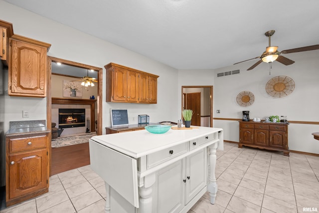 kitchen featuring ceiling fan, brown cabinetry, a center island, a tile fireplace, and visible vents