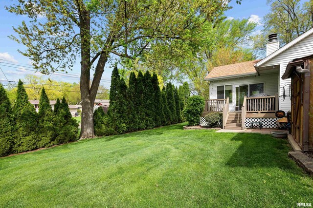 view of front of home with roof with shingles, a front yard, a chimney, and a deck