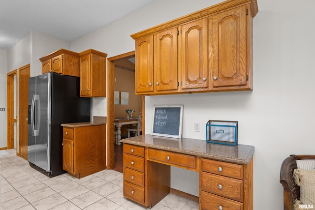 kitchen with built in study area, stainless steel fridge with ice dispenser, brown cabinets, and dark stone counters